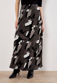 Femme portant une jupe midi noire avec des motifs abstraits en coups de pinceau gris et blancs, assortie à des bottes à talons pointues noires.
