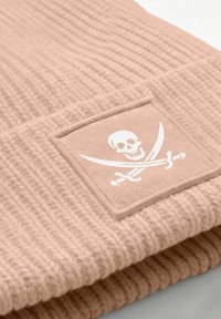 Pink knitted beanie with ribbed texture, featuring a square patch with a white skull and crossed swords design.