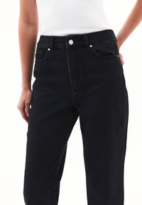 Höga svarta denimjeans med rak ben, framfickor och subtila koppardetaljer på hardwaren. Enfärgade utan mönster.