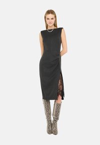 Vestito nero senza maniche, con spacco laterale che mostra dettagli in pizzo e tessuto texturizzato; abbinato a stivali al ginocchio con stampa effetto serpente.