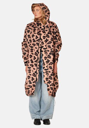 Vrouw met een roze en zwart luipaardprint regenjas met capuchon, lichtblauwe wijde jeans en zwarte schoenen, recht naar voren staand.