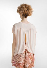 Lyserød kortærmet top med rund halsudskæring, baglås med knude og åbent nøglehul-detalje, kombineret med mønstrede shorts.