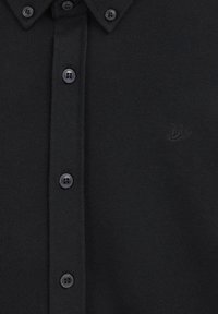 Melna polo krekla ar teksturētu audumu, kas aprīkots ar pogām priekšpusē un piecām saskaņotām pogām. Tam ir smalks izsistu logo uz krūts.