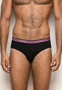 Männlicher Oberkörper, der schwarze Unterhosen mit einem lila Bündchen trägt, auf dem der Markenname "yamamay" auf einem schlichten Hintergrund zu sehen ist.