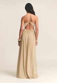 Vestido maxi beige con falda fruncida, tirantes de espagueti en cruz y diseño de espalda descubierta. Hecho de un tejido ligero y texturizado.