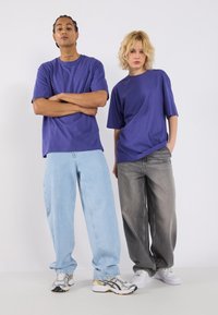 Divi indivīdi valkā pārspīlēti lielas purpurkrāsas T-krekli. Viens tērpies gaiši zilās džinsās, otrs tumši pelēkās. Apavi ar sudraba akcentiem.