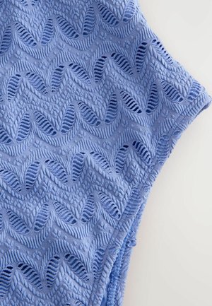 Teksturirano modro blago z valovitim vzorcem, ki vključuje izmenično dvignjene in ravne dele, prikazuje mehak, zapleten dizajn ter podrobnosti o ventilaciji.