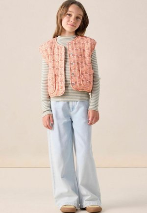 Gehaakte oranje vest met een textuurpatroon, ronde halslijn en twee voorkruiden over een gestreept lange mouwen top en lichtblauwe wijde jeans.