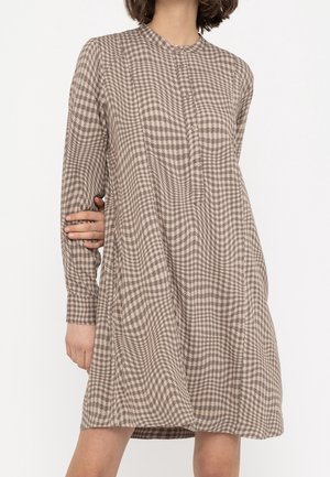 Femme portant une robe beige et marron à motif pied-de-poule, manches longues, longueur genou, avec des boutons sur le devant.