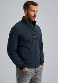 Dunkelblaue Softshell-Jacke mit hohem Kragen, durchgehendem Reißverschluss, Seitentaschen und gerippten Bündchen. Glatte Textur und modernes Design.