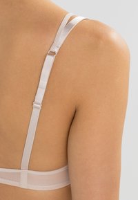 Tirante de sujetador de color rosa claro con un acabado brillante, hardware ajustable y una banda sheer de textura suave. Diseño simple y limpio enfocado en la funcionalidad.