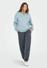 Felpa oversize azzurro chiaro con la scritta "THE LAY" in bianco e pantaloni della tuta grigio scuro. Entrambi sono realizzati in morbido tessuto di cotone.
