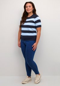 Modrý a námořnický pruhovaný krátký rukáv top spárovaný s modrými skinny džíny a béžovými teniskami. Top má kulatý výstřih a žebrovaný lem.