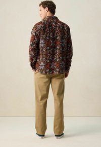 Brown patterned long-sleeve shirt with floral motifs, paired with beige straight-leg pants and black sneakers with white soles.