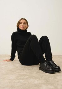 Svart polotröja och matchande joggers i mjukt material; modellen bär svarta läderskor med snörning och tjock sula.