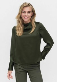 Tummanvihreä satiinipaita, jossa on korkea kaulus, pitkät hihat ja napakat hihansuut. Silkkinen pinta, hieman pyöristetty helma. Yhdistetty saman sävyisiin housuihin.