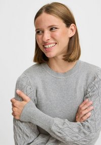 Maglione grigio lavorato a maglia con scollo a costine e motivo a trecce sulle maniche, con polsini aderenti e una texture morbida.