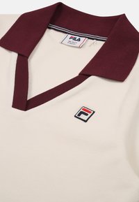 Polo shirt color crema con colletto a coste bordeaux, dotato di un logo Fila ricamato in rosso e blu sul lato sinistro del petto.
