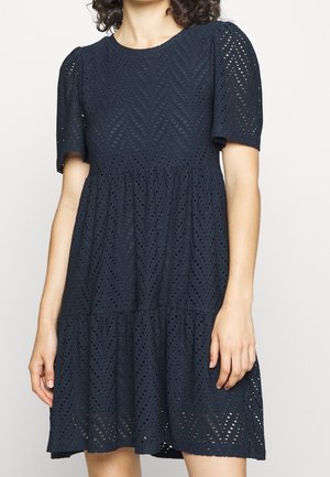 Donkerblauwe jurk van oogjesstof met zigzagpatronen, korte pofmouwen en een gelaagde rokontwerp.