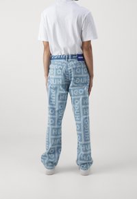 Jeans azul claro con logos impresos en toda la prenda y una cinturilla azul contrastante. Presenta un ajuste regular y un diseño de cinco bolsillos.