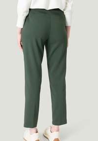 Pantalon vert ajusté au style épuré, avec une texture lisse et de discrètes poches arrière, associé à des baskets beiges.