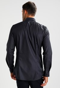 Black long-sleeve shirt with a fitted design, smooth texture, button cuffs, and a classic collar, shown from the back.