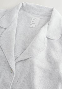 Lichtgrijs pyjamashirt met een subtiel textuurpatroon, knoopsluiting en klassiek kraagontwerp. Merklabel zichtbaar in de hals.