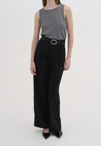 Top sin mangas gris acanalado combinado con pantalones negros de cintura alta. El conjunto está cinchado con un cinturón negro que presenta una hebilla plateada. Zapatos negros de punta.