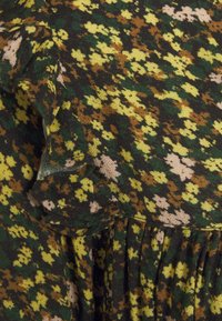 Tissu vert foncé avec un petit motif floral jaune, marron et beige et des fronces texturées créant des détails à volants.
