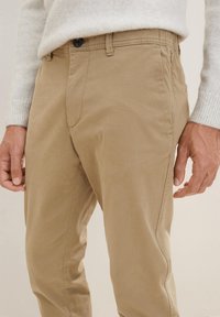 Khaki chinos wykonane z lekkiego materiału, z prostym krojem, zapinane na guzik oraz z bocznymi kieszeniami, z widocznymi detalami przeszyć.