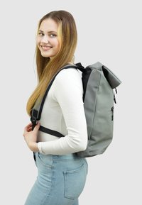 Grijze oprolbare rugzak gemaakt van duurzaam materiaal, met verstelbare zwarte schouderbanden, een voorvak met rits en een strakke, moderne uitstraling.