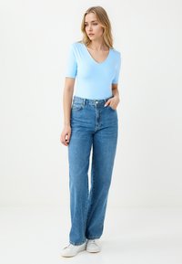 Lichtblauw kortemouwen bodysuit gecombineerd met hoge taille, rechte spijkerbroeken en witte sneakers. Minimalistisch ontwerp met een V-hals.