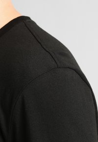 Black cotton t-shirt featuring a round neckline and short sleeves. Smooth texture with seams visible on the shoulder and sleeve edges.