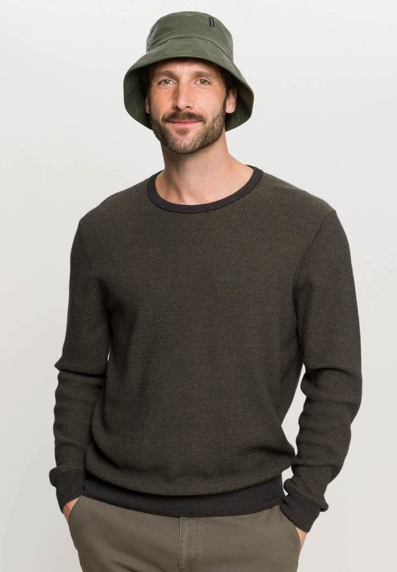 Pullover in maglia di un verde scuro e testurizzato, con un colletto a girocollo e polsini a coste, abbinato a un cappello a secchiello verde coordinato.