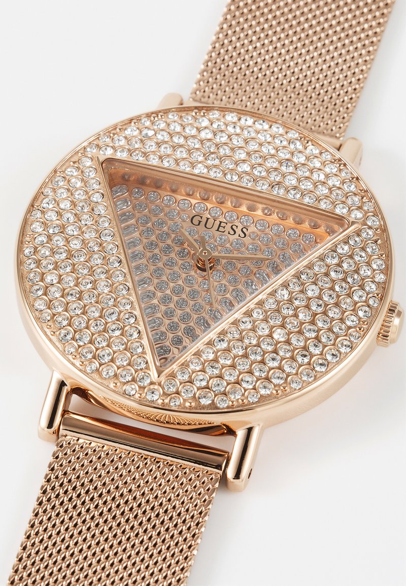 Montre en or rose avec un cadran triangulaire orné de cristaux et un bracelet en maille. Elle présente un cadran minimaliste avec des aiguilles des heures et des minutes.