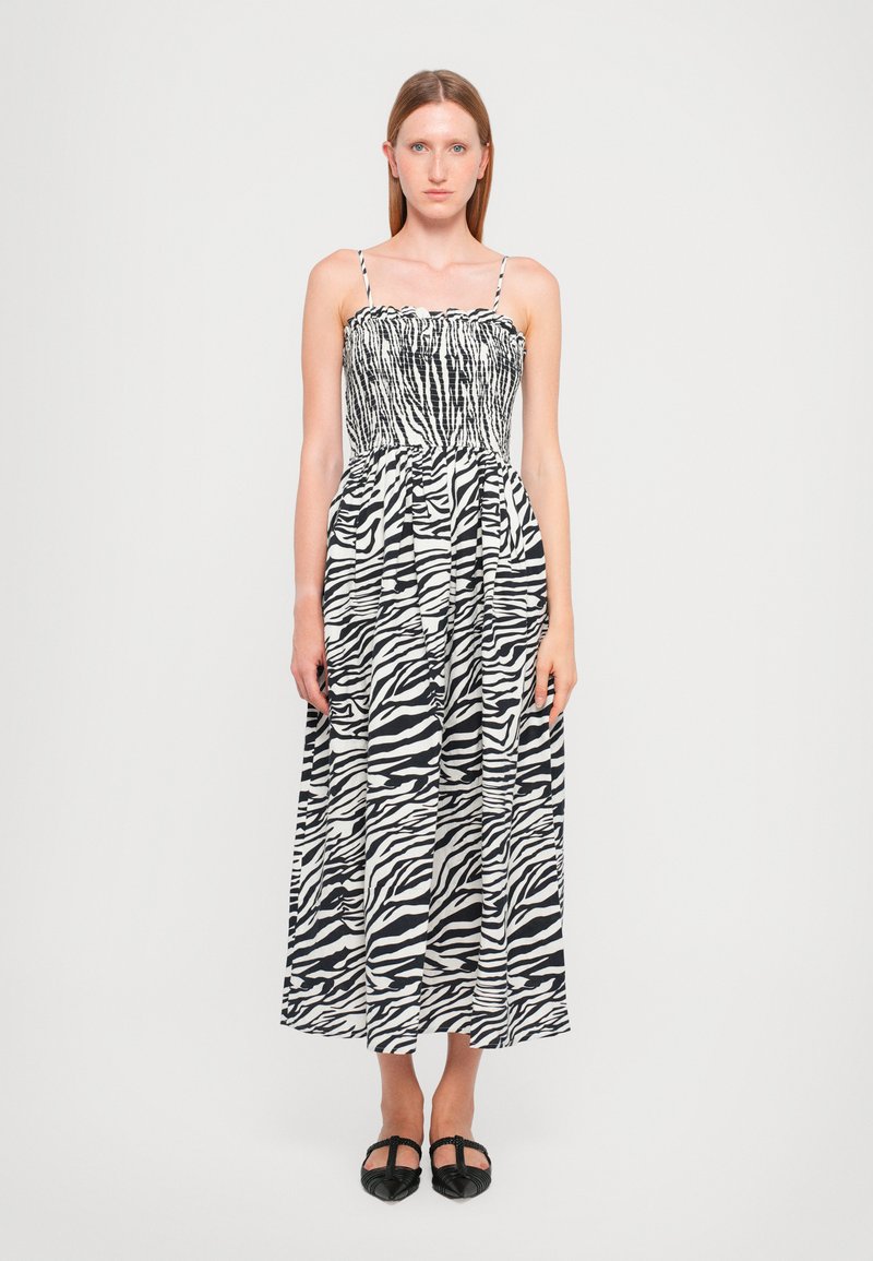 Maxikjole i sort og hvid zebra-mønster, med spaghettistropper, en smocked bodice og en flydende nederdel med folder. Sorte flade sko.