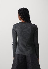 Black long-sleeve top with a textured, ribbed finish, featuring a crew neck and slim fit, paired with a dark quilted skirt.