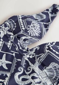 Tissu bleu marine avec des imprimés blancs représentant la vie marine, incluant pieuvre, étoile de mer, coquillages et corail dans des motifs carrés encadrés.