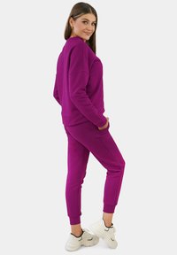 Lila Sweatshirt und passende Jogginghose aus weichem Material. Das Sweatshirt hat tief angesetzte Schulternähte; die Jogginghose hat elastische Bündchen und Taschen.