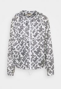 Lekka kurtka z kapturem w kolorze białym z czarnym geometrycznym wzorem gwiazd. Posiada zamek błyskawiczny z przodu oraz sznurki ściągające na dolnym brzegu i przy mankietach.