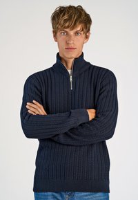 Navyblau gestrickter Pullover mit hohem Kragen und halbem Reißverschluss, ausgestattet mit einem strukturierten Muster und Rippbündchen an den Ärmeln und am Saum.