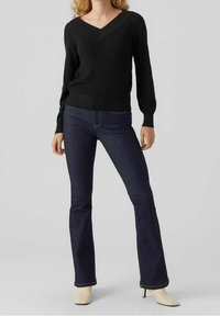Pullover nero a costine con scollatura a V, abbinato a jeans svasati blu scuro e décolleté beige a punta. Design semplice e aderente.