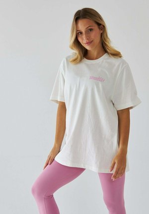Biała, oversize'owa koszulka z różowym napisem "pilates princess", w zestawie z dopasowanymi różowymi legginsami. Prosty design, krótkie rękawy, miękka faktura.