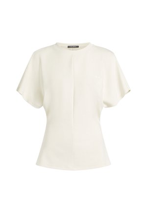 Haut crème à manches courtes avec un col rond, présentant une couture centrale et un accent logo subtil. Texture douce et silhouette décontractée.