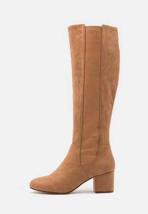 Botte haute pour femme en daim marron clair avec talon bloc et panneau élastique côtelé le long du mollet, vue de côté sur fond blanc.