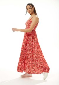 Red floral maxi dress with spaghetti straps, gathered bodice, and flowy skirt. Worn with white sneakers, featuring small white and yellow flowers.