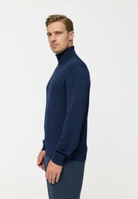 Tengerészkék garbó pulóver sima kötött anyagból, hosszú ujjakkal és testhezálló fazonnal, bordás mandzsettákkal és gallérral.