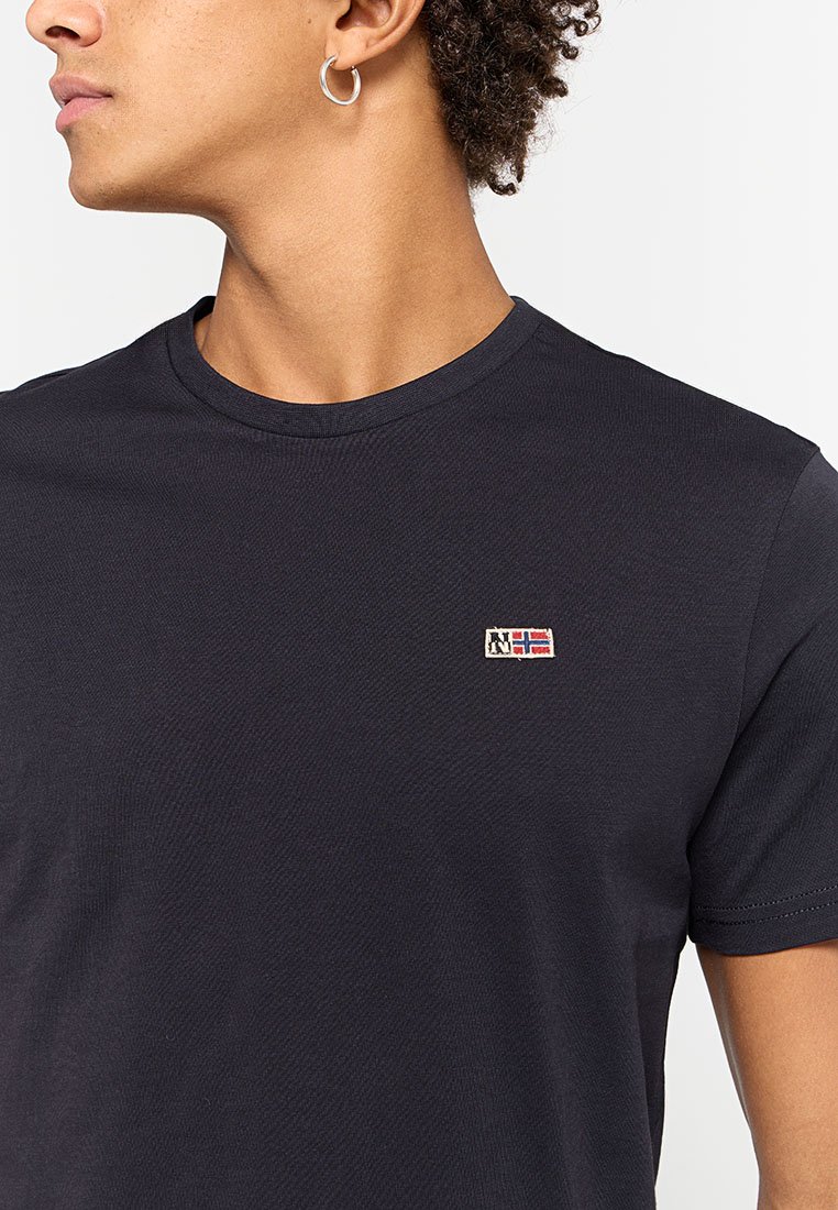 Maglietta di colore blu navy realizzata in tessuto testurizzato, con colletto rotondo e un piccolo logo della bandiera ricamato sul lato sinistro del petto.