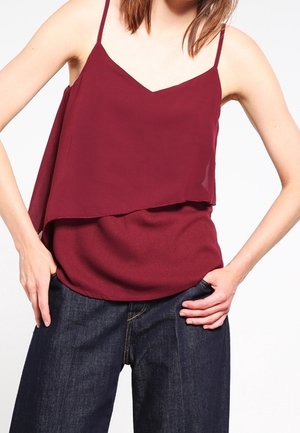 Top senza maniche bordeaux con design a strati, dotato di scollatura a V e spalline sottili, abbinato a jeans a gamba larga blu scuro.