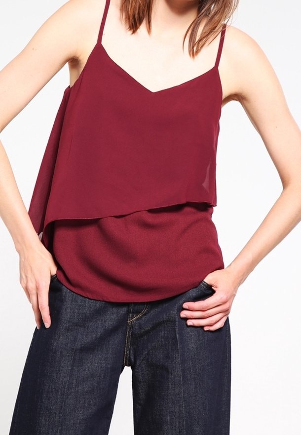 Top senza maniche bordeaux con design a strati, dotato di scollatura a V e spalline sottili, abbinato a jeans a gamba larga blu scuro.